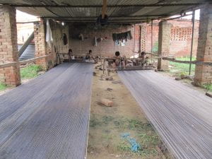 Image of children weaving carpets under aluminum shade covers on brick columns.