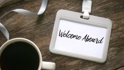 Coffee mug and employee ID card on desk. Employee ID card reads "welcome aboard: