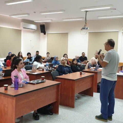 Man standing and holding microphone speaking to students seated in classroom