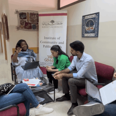 Seated woman speaking to group of four seated students in a hallway at Birzeit University Institute of Community and Public Health