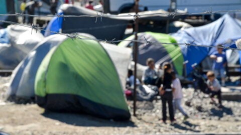 Blurred camping tents and children behind barbed wire at Idomeni refugee camp, Greece.