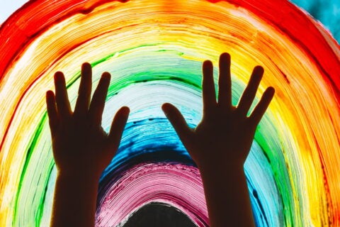Close-up photo of child's hands touch painting rainbow on window.