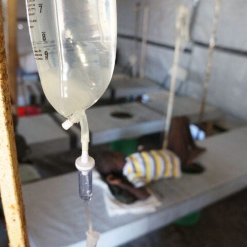Image of IV fluid bag hanging fro rusty metal pole in rural area clinic. Credit: Rebecca Rollins, Partners in Health