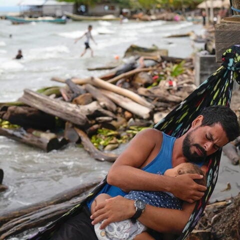 Man sitting on hammock with baby in his arms. AP.