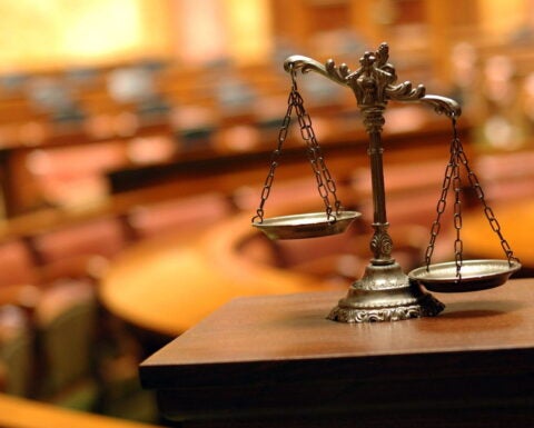 Symbol of law and justice, photo of scale against blurred background of auditorium with wooden seats.