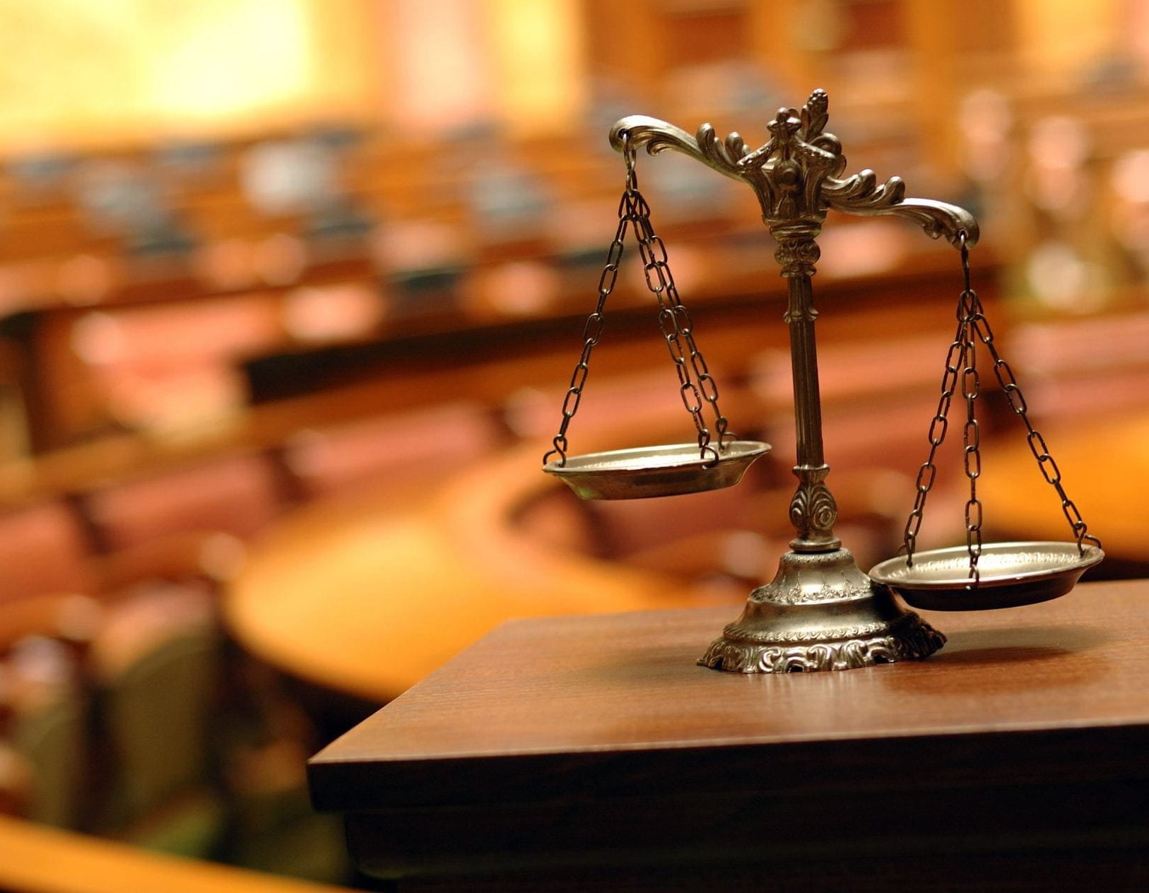 Symbol of law and justice, photo of scale against blurred background of auditorium with wooden seats.