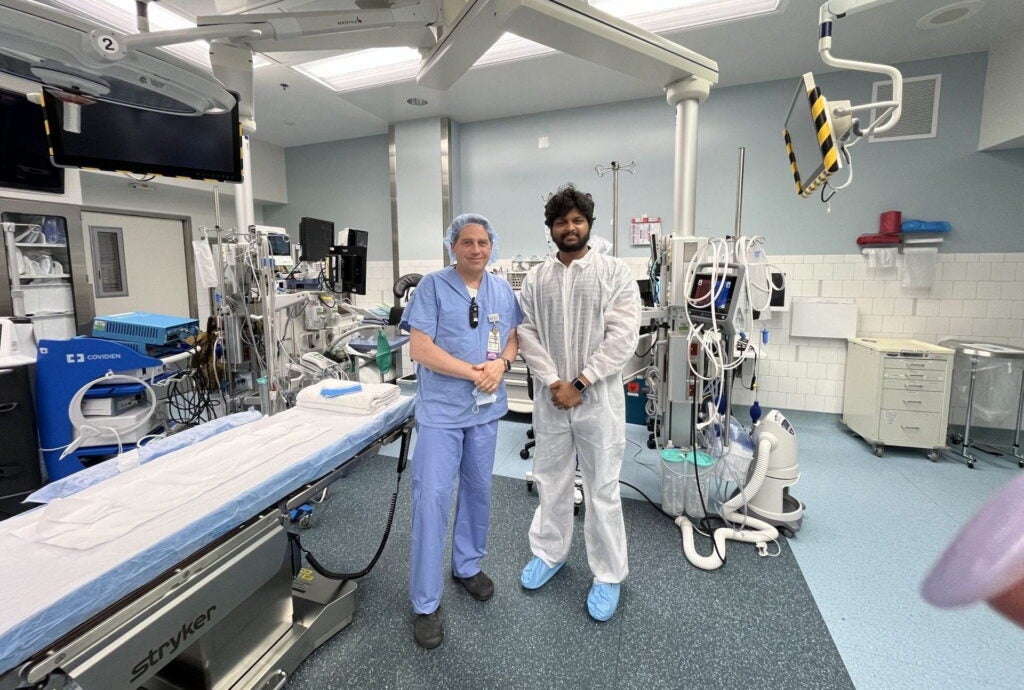 Lexi co-founder Siddharth UR posing for photo in white scrubs alongside doctor in operating room.