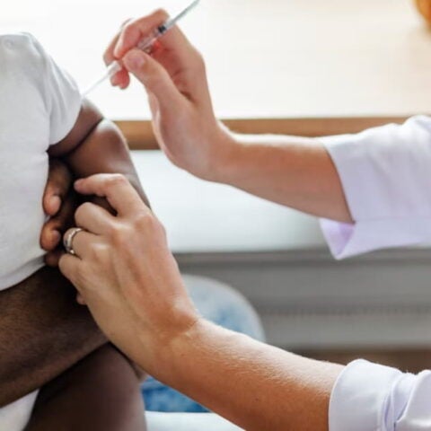 Photograph of young child receiving a vaccine while sitting on the lap of an adult.
