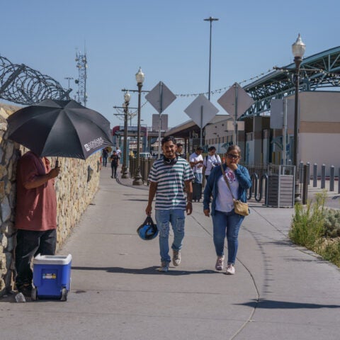 A vendor sells bottled water while shading himself with an umbrella at the exit of the Paso del Norte International Bridge during triple-digit temperatures in El Paso on Aug. 7. Photo by Paul Ratje.