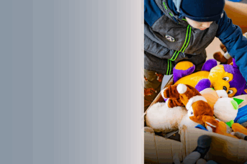 Image of child in winter jacket and hat picking toys out of cardboard boxes.
