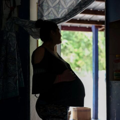 Photo of pregnant woman standing in dark doorway, looking outside.