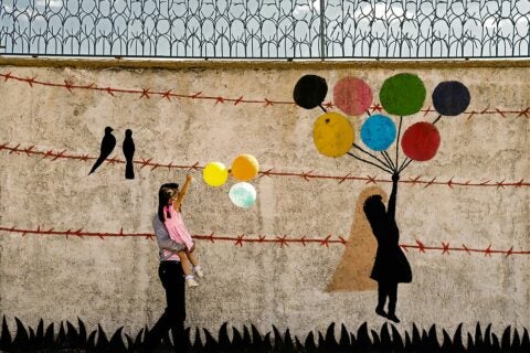 Photo of child holding balloons by a wall with graffiti of a child holding balloons.