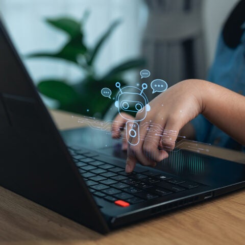 A child types into a keyboard of a laptop, with decorative drawings above it, representing artificial intelligence.