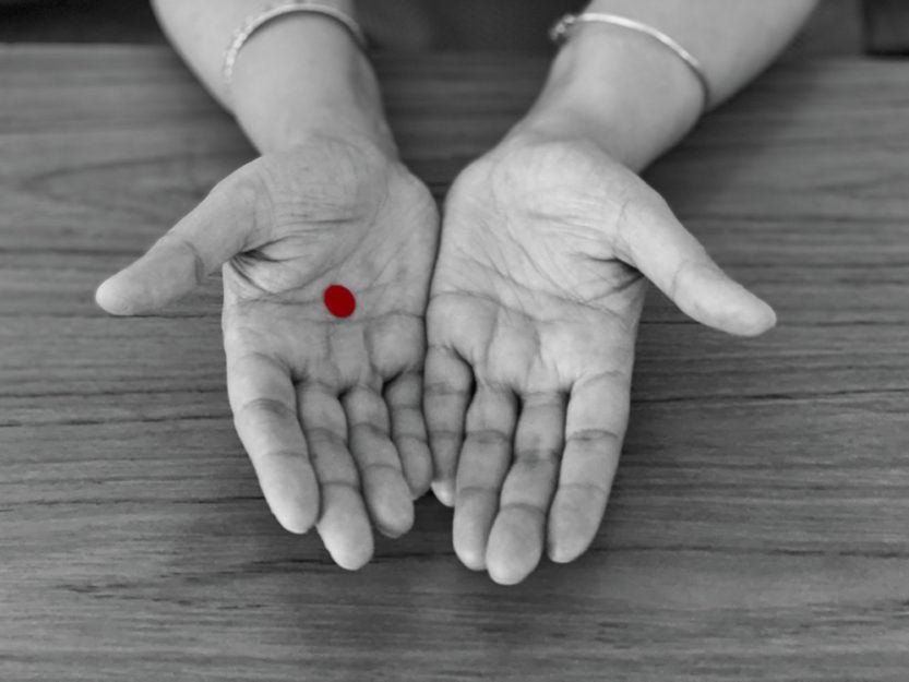 Photo of outstretched hands, one with a red dot