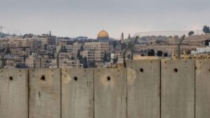 View of the Dome of the Rock amid concrete buildings beyond a concrete and barbed wire fence, Jerusalem.