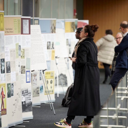 Woman in black coat and sneakers looking at the Legacies of Eugenics exhibition posters at the Martin Center on April 6, 2023.
