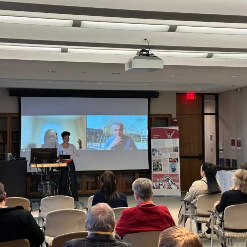 Gracyelle Costa Ferreira, PhD, speaking during the opening of the exhibition “We Are Not Alone”: Legacies of Eugenics at Harvard's Countway Library. Evelynn Hammonds, PhD, and Marius Turda, PhD, are visible on Zoom on the screen behind her.