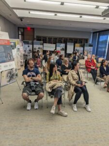 Attendees of the opening of the exhibition “We Are Not Alone”: Legacies of Eugenics at Harvard's Countway Library listening to speaker presentations. Audience is seated with some of the exhibition posters and retractable banners visible in the background.