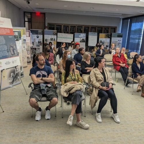 Attendees of the opening of the exhibition “We Are Not Alone”: Legacies of Eugenics at Harvard's Countway Library listening to speaker presentations. Audience is seated with some of the exhibition posters and retractable banners visible in the background.