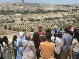 Man speaking to group of students standing outside with Jerusalem and the Dome of the Rock visible behind them