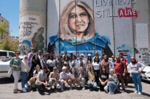 Student cohort of the inaugural Palestine Program for Health and Human Rights Social Medicine Summer course, July 2023. Students standing and seated on the street in front of wall with mural of woman with head covering.