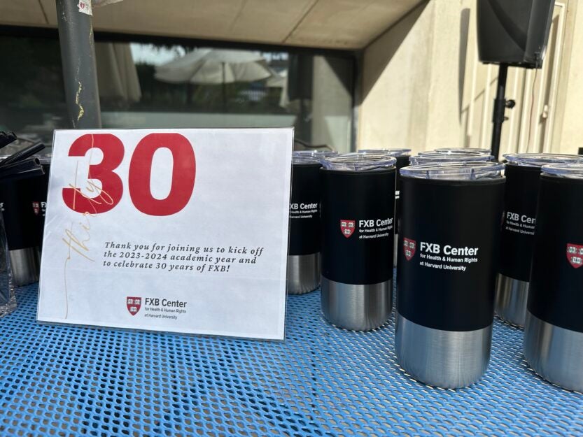 Printed sign in transparent vinyl holder thanking attendees for joining FXB's 30th anniversary celebration next to black tumblers with FXB logo.