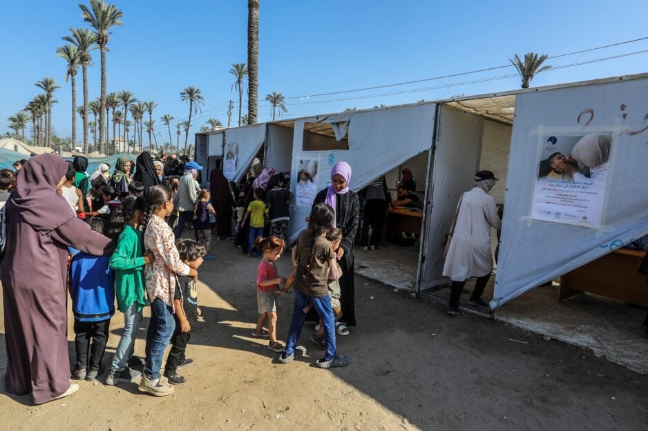 Photo of children lining up outside white UNRWA tents to receive polio vaccines in Gaza, September 2024. Photo credit: Anas Mohammed.